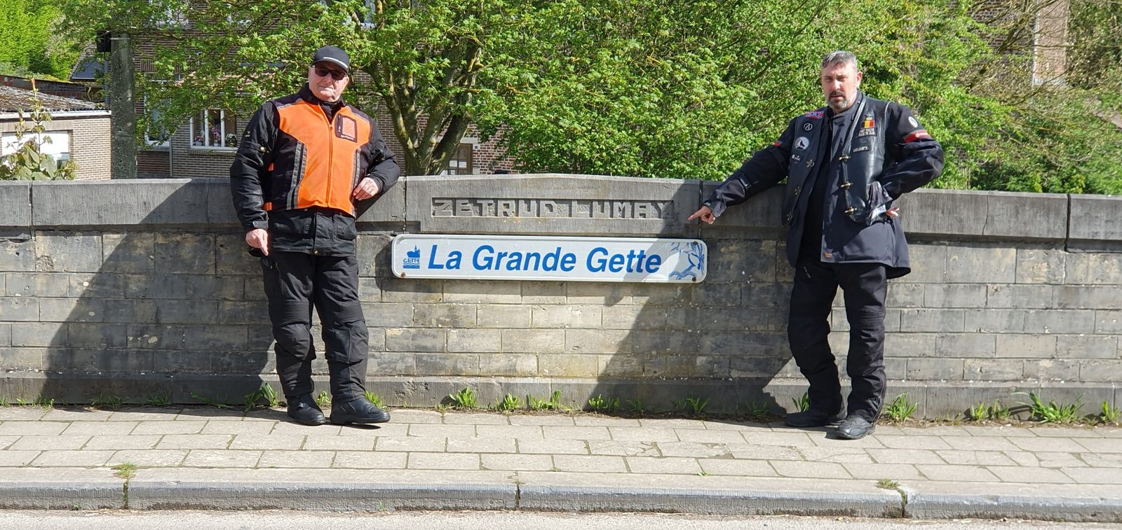 Twee rijders staan naast een brugmuur met het bordje La Grande Gette.